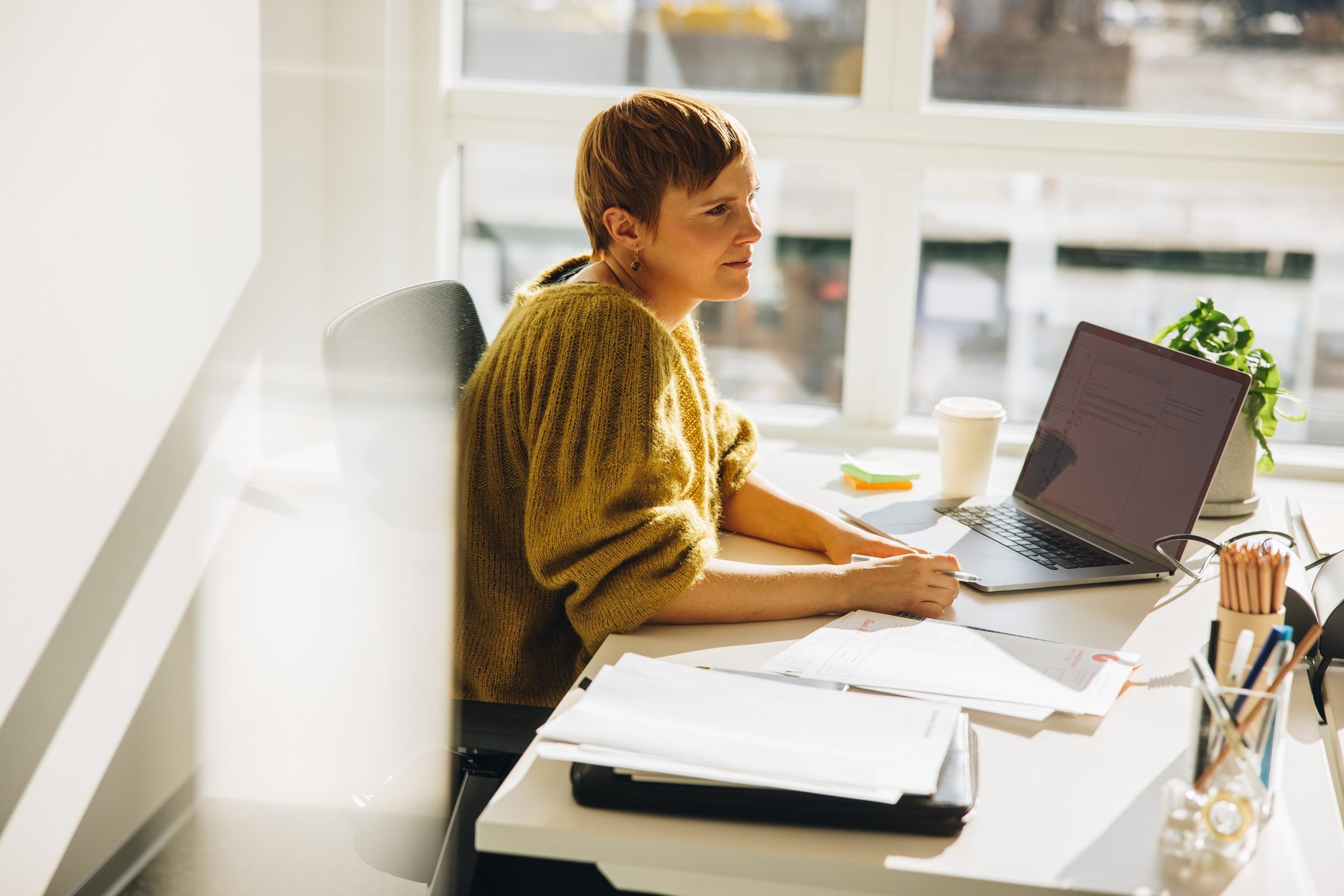 Eine Lehrerin arbeitet am Fenster mit Laptop und Unterlagen